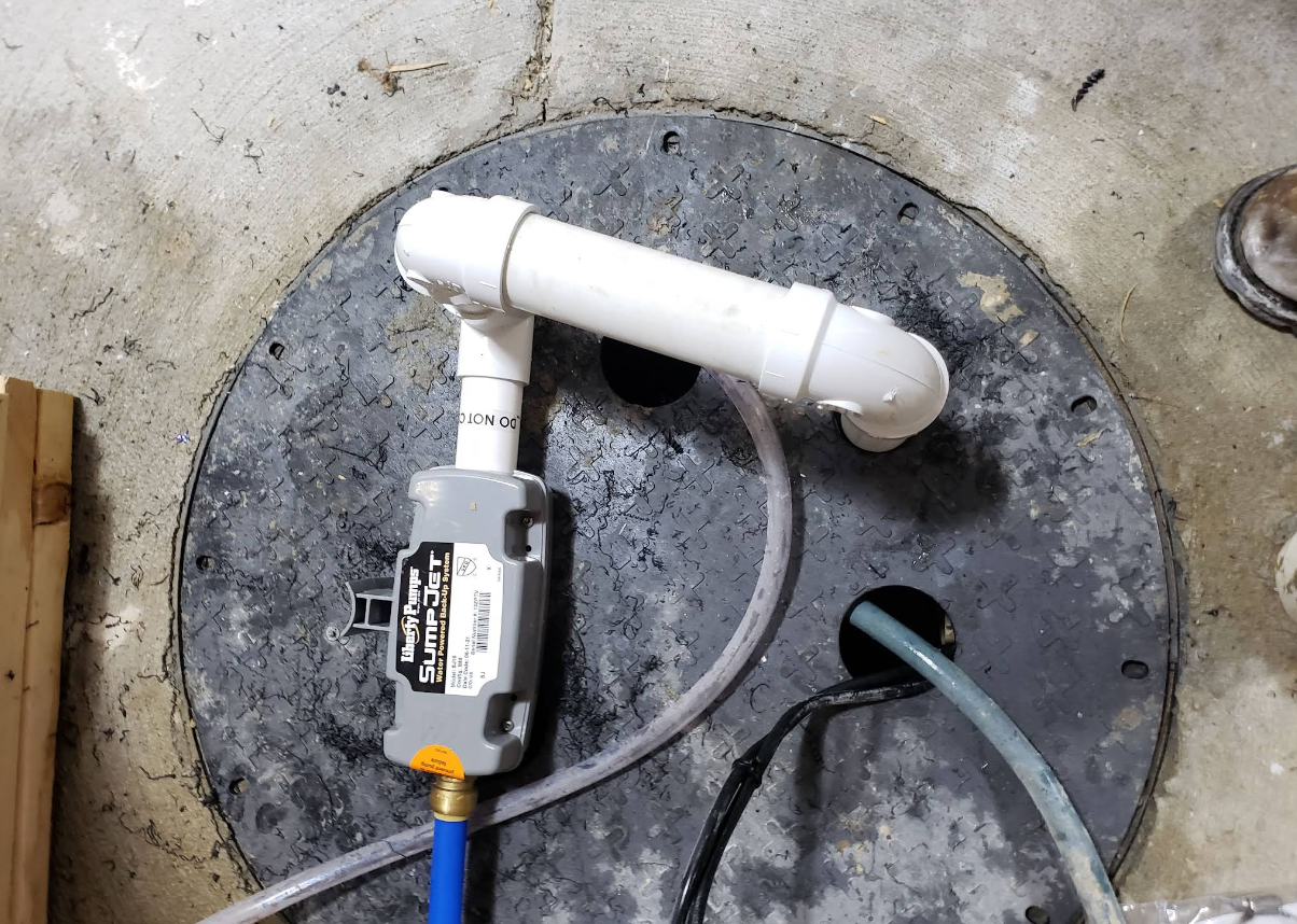 White PVC pipe and gray pump installed in a concrete floor opening.