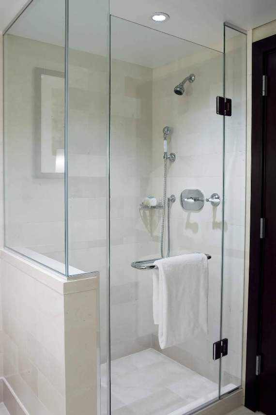 Glass-enclosed walk-in shower with chrome fixtures and a white towel hanging on the door.