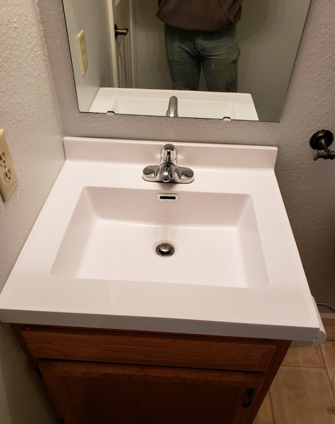 Bathroom sink with white countertop and mirror above a wooden vanity.