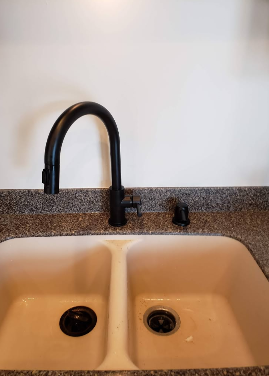 Double-basin kitchen sink with black faucet and speckled countertop against a plain wall.
