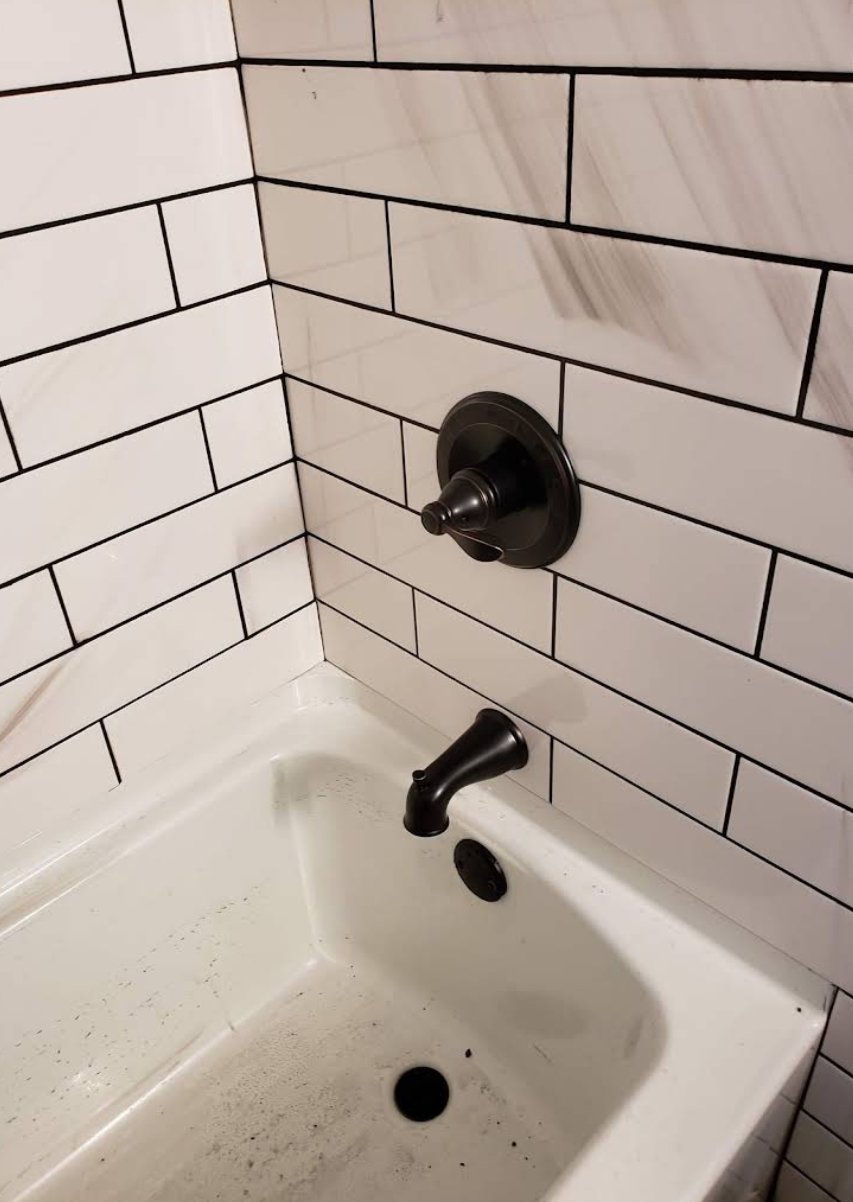 Bathroom sink and tub faucet against white subway tile, with exposed plumbing fixtures.