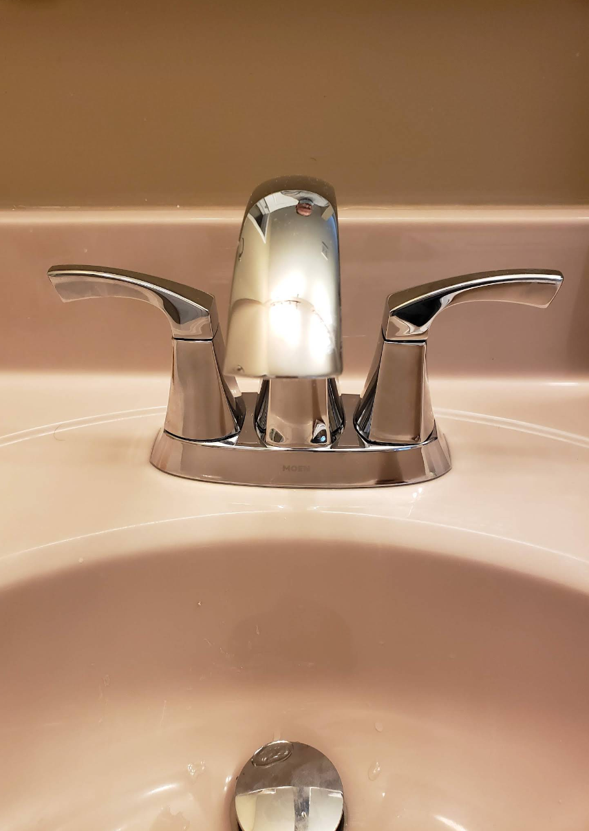 Chrome bathroom faucet over a white sink with a beige countertop background.