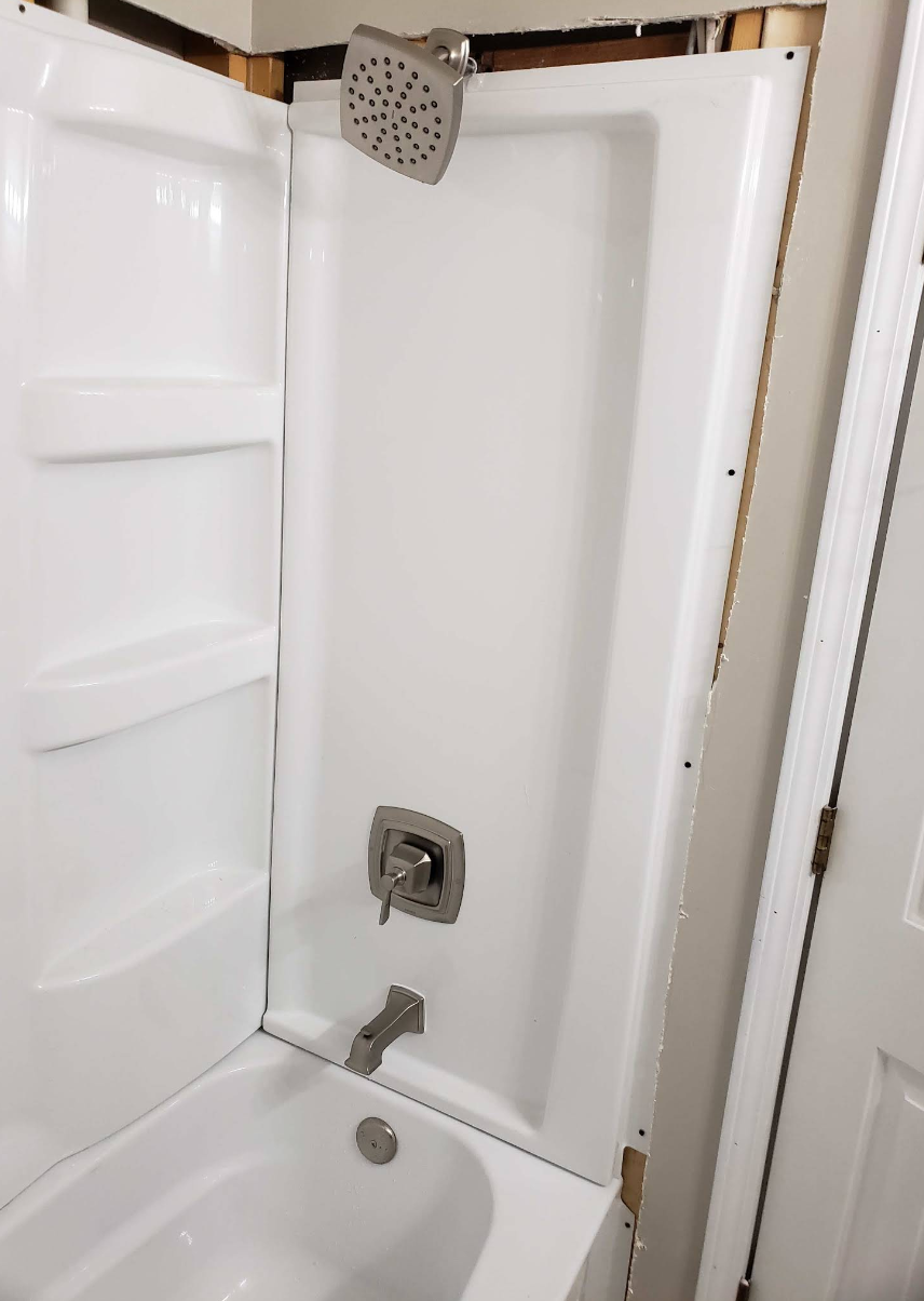 Open shower stall with white walls, showerhead, faucet, and built-in shelf.