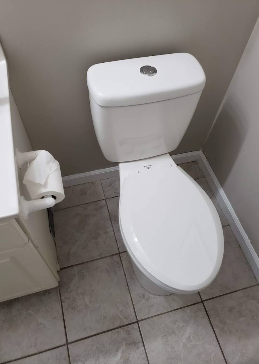Small bathroom with a white toilet beside a toilet paper holder and tiled floor.