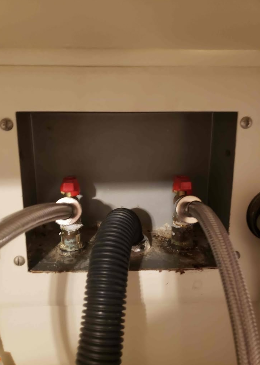 Under-sink plumbing access panel with two red shutoff valves and connected hoses.