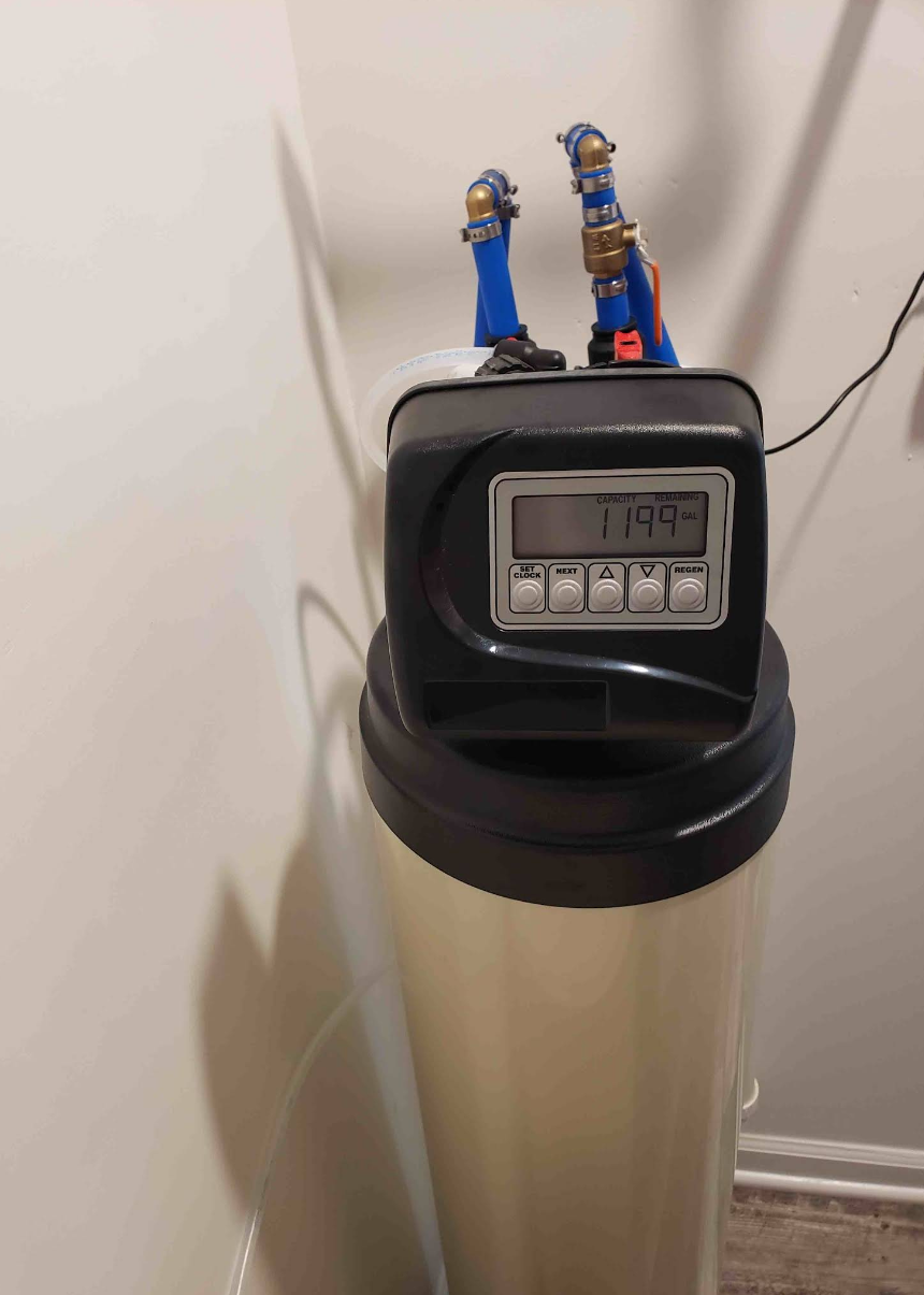 Water softener tank with digital control head and blue valves in a corner.