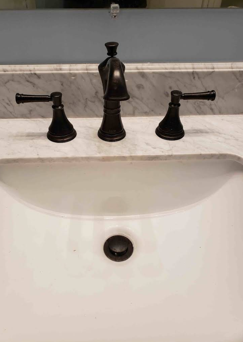 Bathroom sink with black faucet and handles above white porcelain basin.