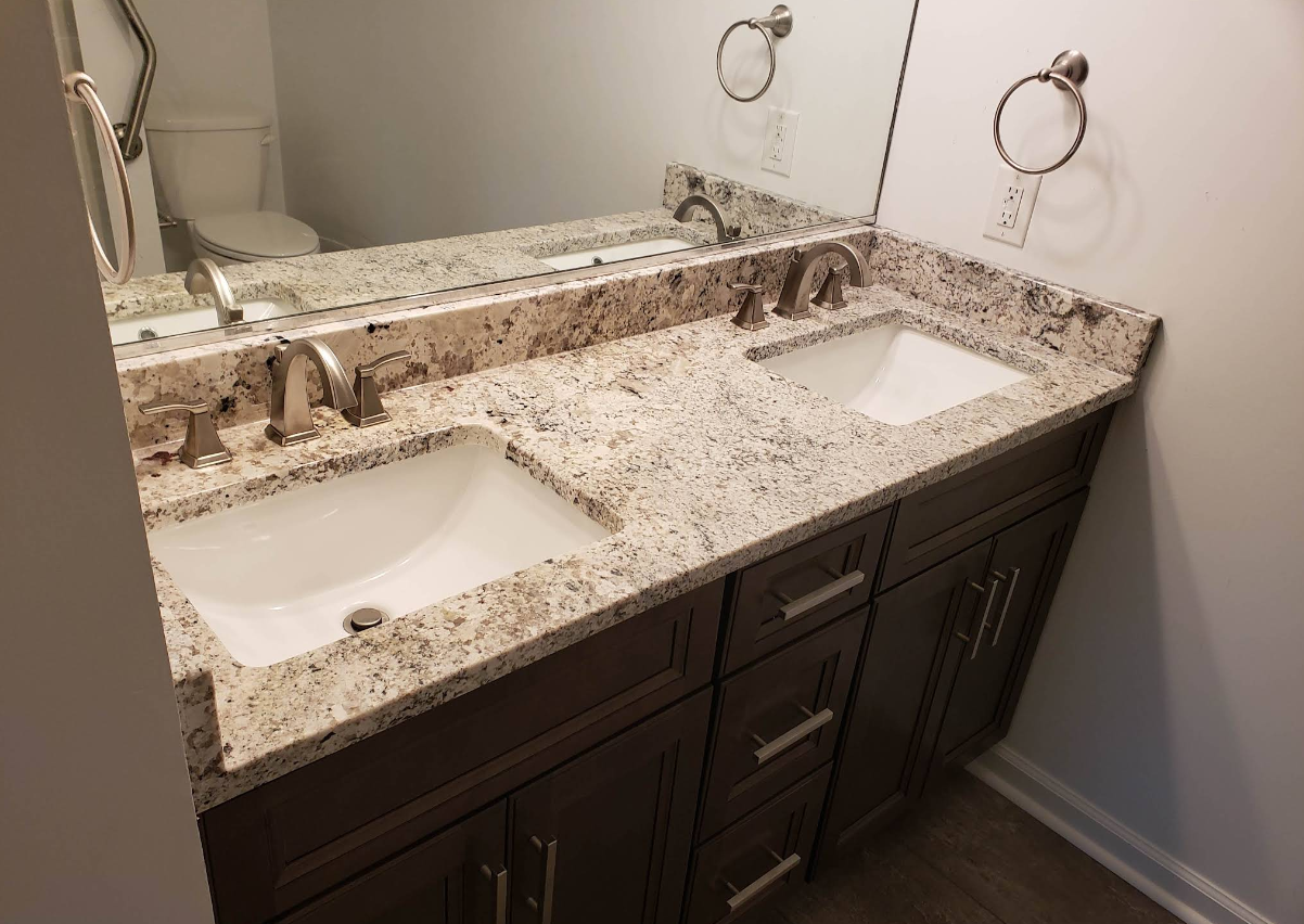Double vanity bathroom sink with granite countertop, dark wood cabinets, and wall mirrors.
