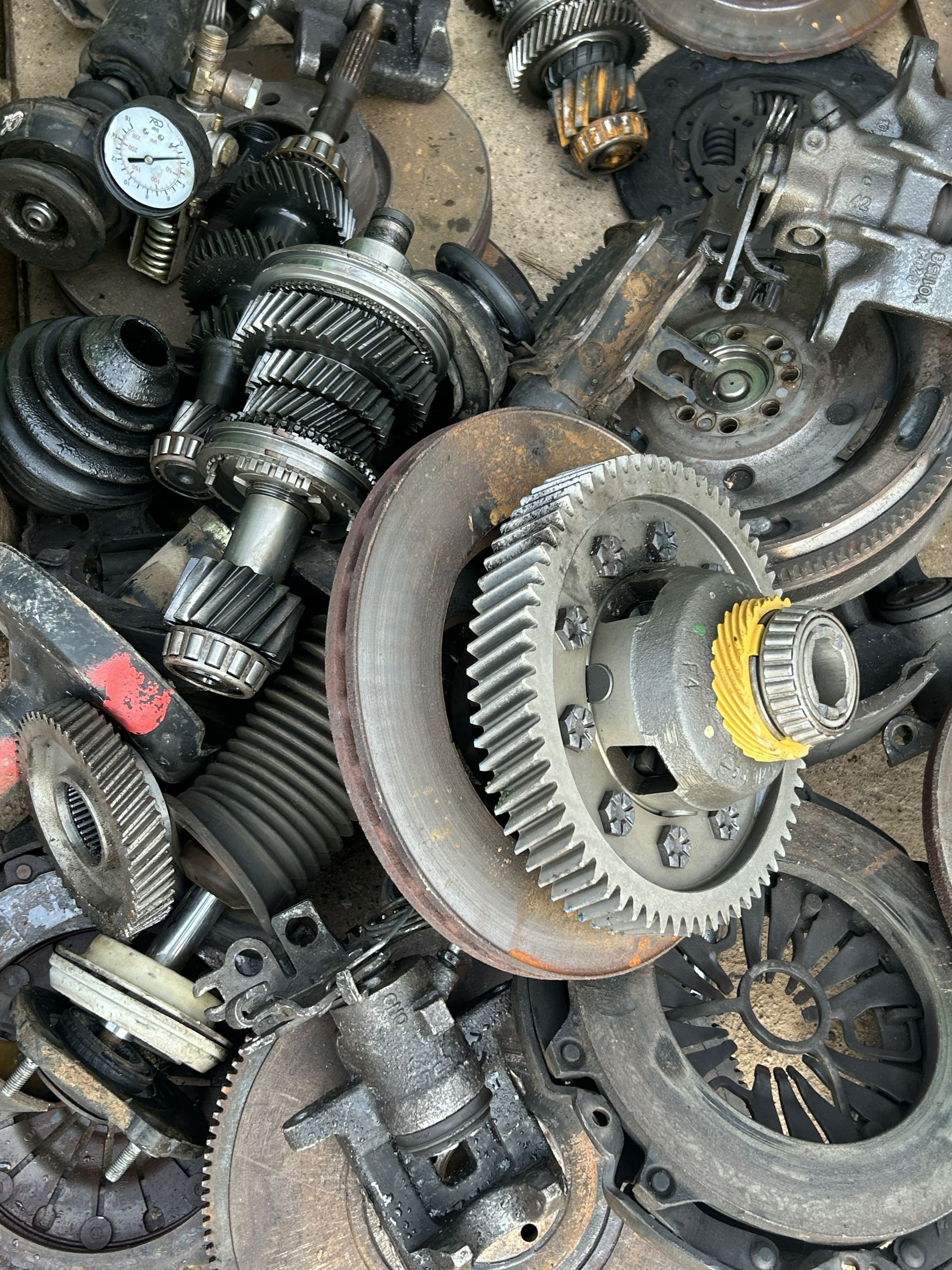 Green basket filled with assorted car parts and tools, including metal gears, springs, and filters.