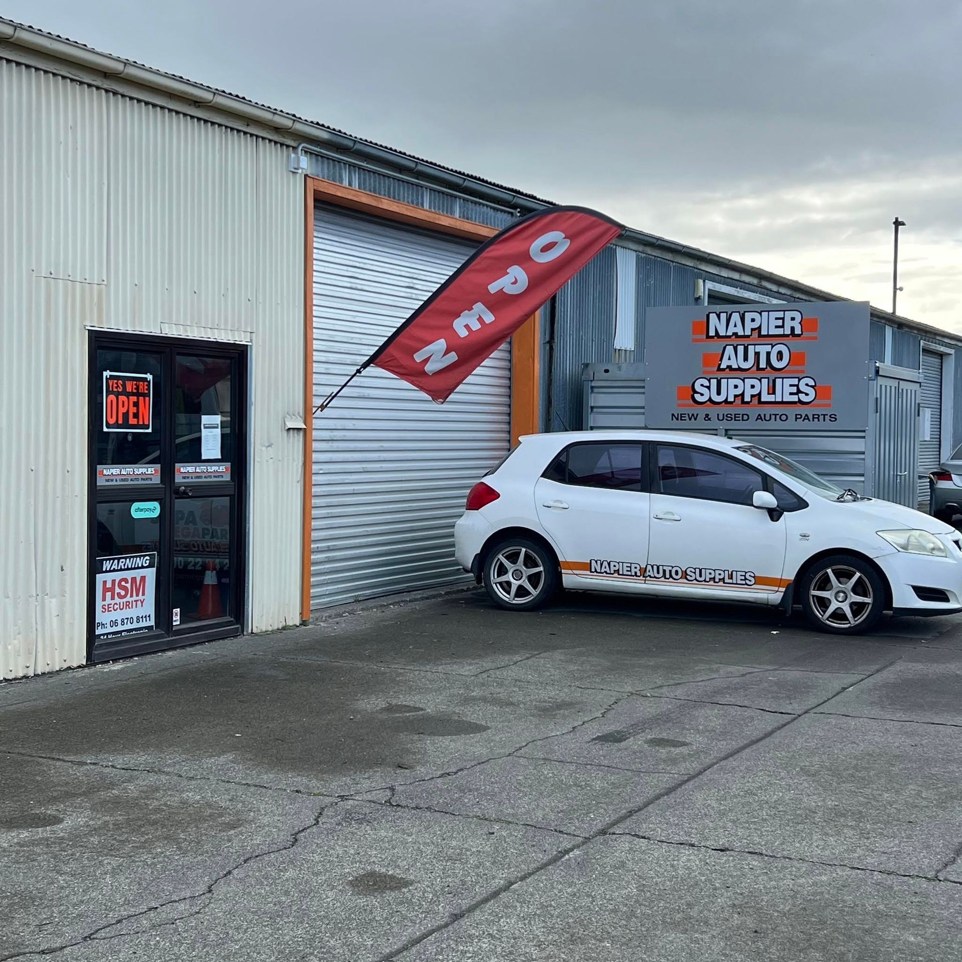 White hatchback parked outside Napier Moto Supplies with a red banner over the roller door.