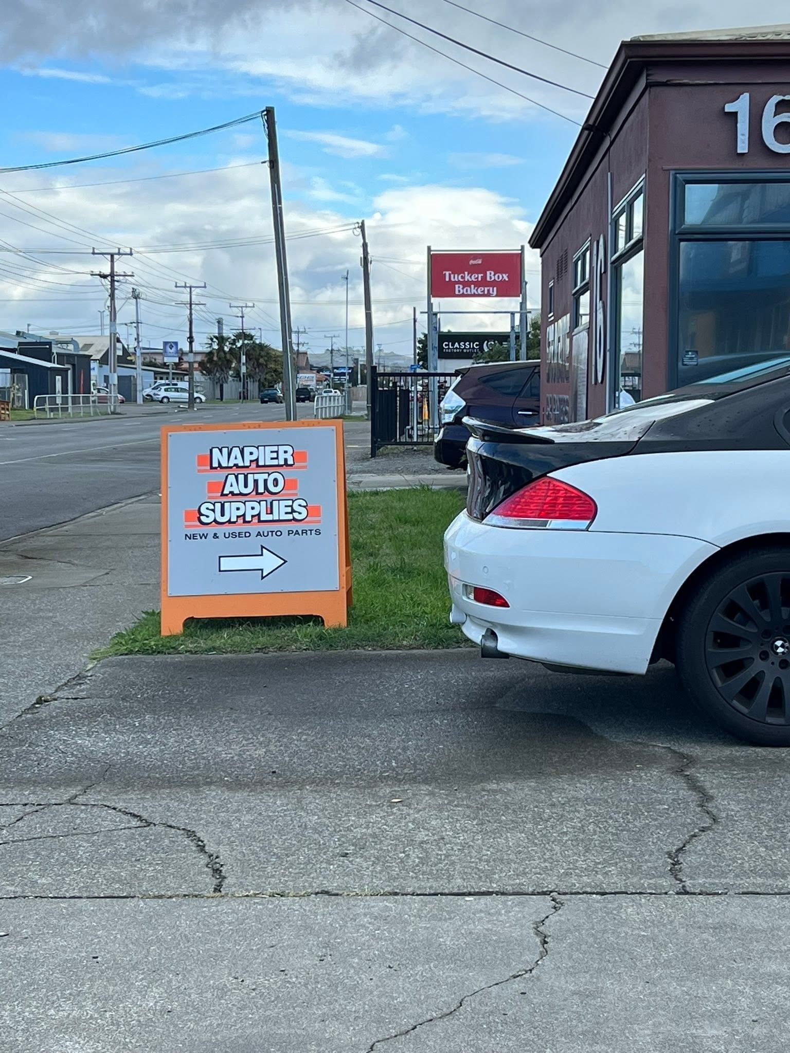 Orange sidewalk sign beside parked white car outside a building on a street.