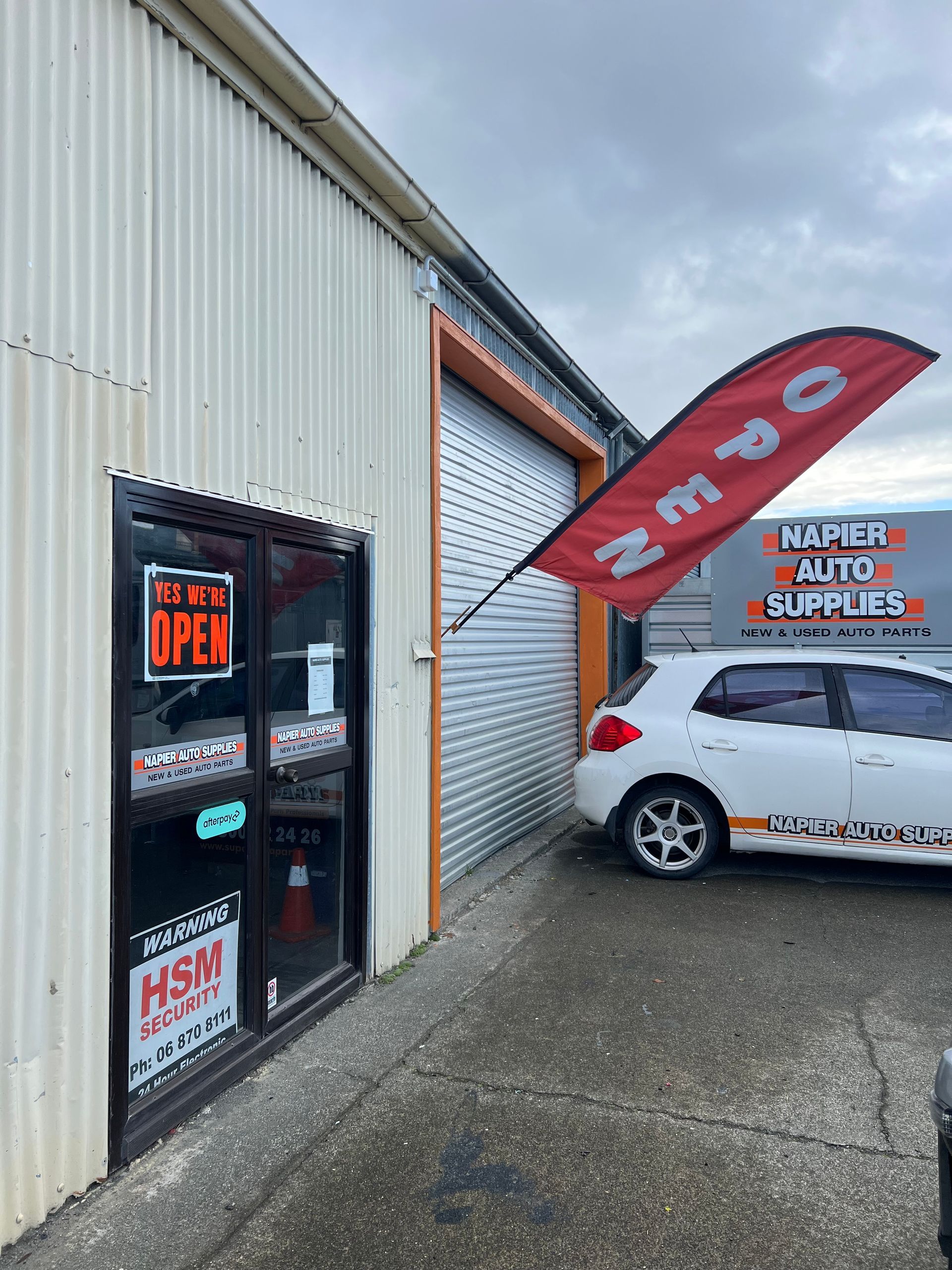 Auto repair shop entrance with open red canopy sign and parked silver car beside a white roll-up door