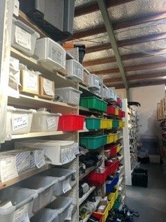 A storage room aisle with stacked plastic bins on metal shelves, labeled and sorted by color.