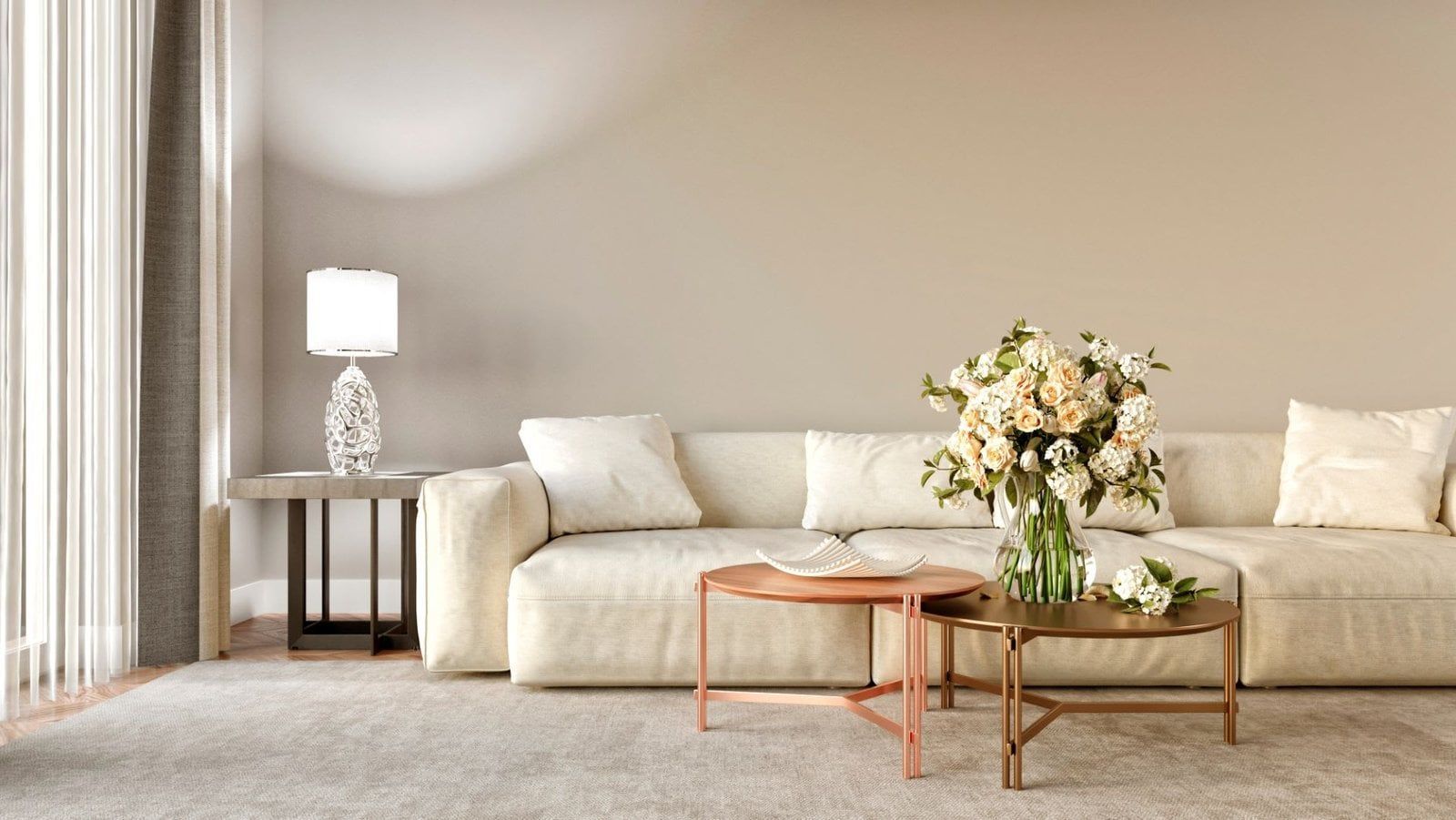 Beige living room with a cream-colored couch, flowers, two round coffee tables, and a lamp on a side table.
