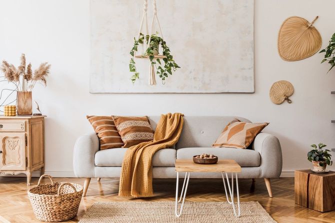 Living room with a gray sofa, brown pillows, and a yellow throw. Features a woven rug, wooden furniture, and plants.