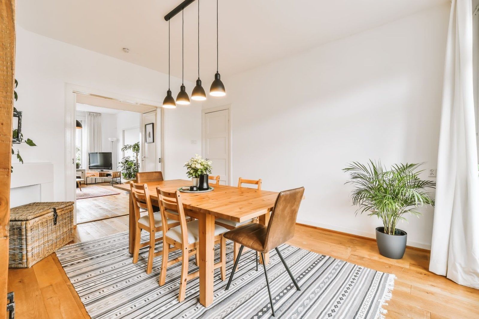 Dining room with wooden table, chairs, rug, and hanging lights.