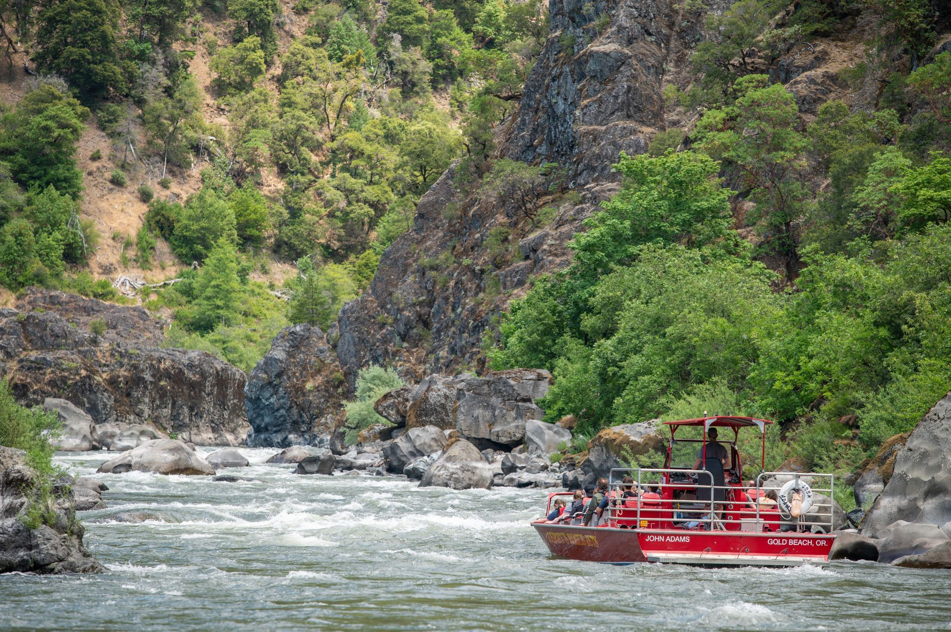 a jet boat going slowly up the rogue river surrounded by trees and cliffs