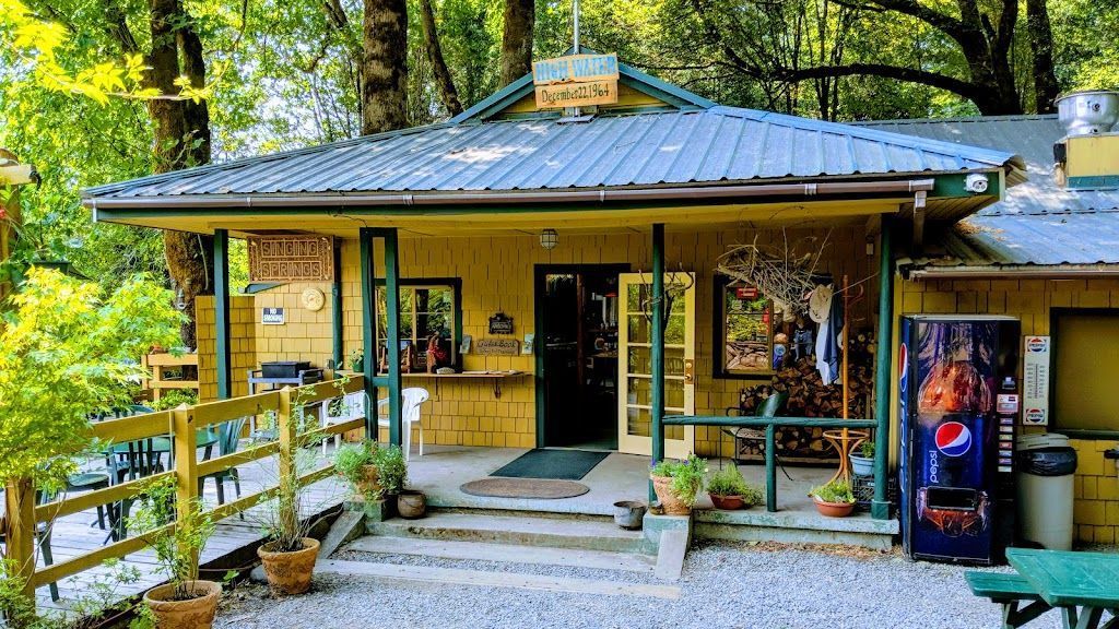 exterior photo of the Singing Springs Resort showing yellow building with front porch area and a drink machine