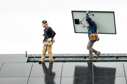 Two workers installing a solar panel on a rooftop.