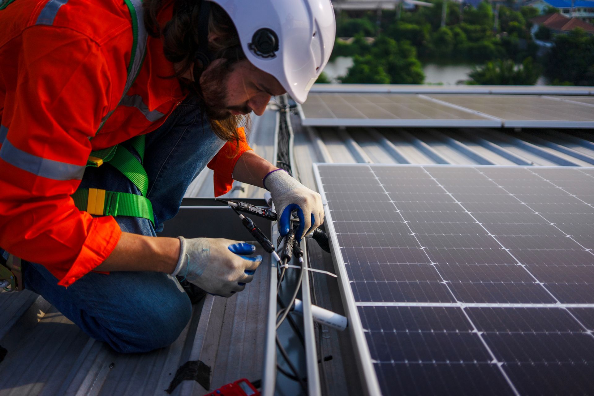 Worker in orange jacket installing equipment beside rooftop solar panels