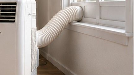 Detalle de la manguera de expulsión de un aire portátil conectada a la ventana para retirar correctamente el calor del condensador.
