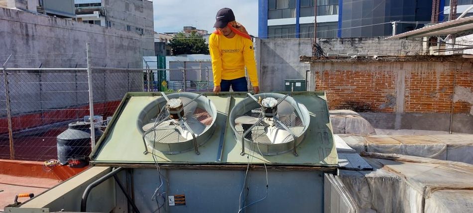 Un hombre con una camiseta amarilla está parado en lo alto de un tejado con dos fans.