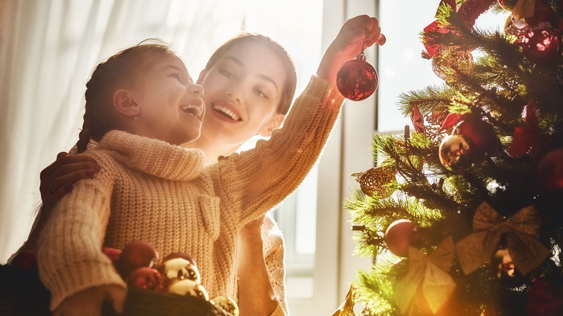 mother helping her daughter hang christmas tree ornaments