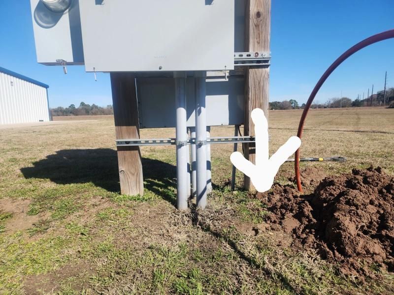 Electrical conduit and wiring near a utility pole, with dirt mound and red cable visible.