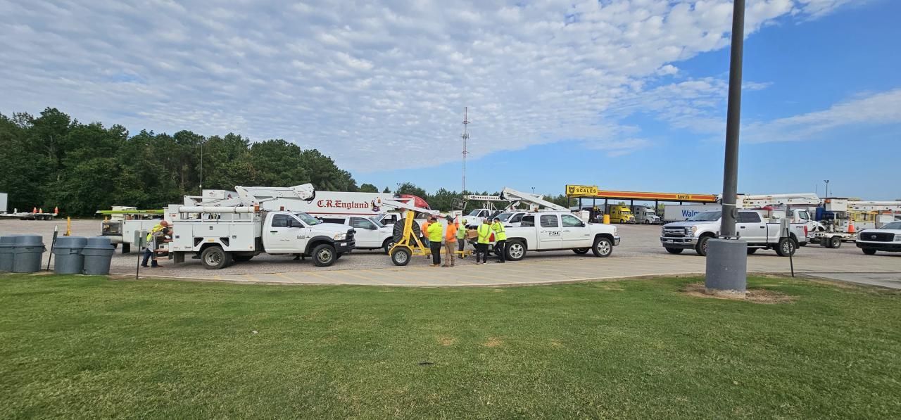 Utility trucks and crew standing on grass near a gas station. Cloudy sky.