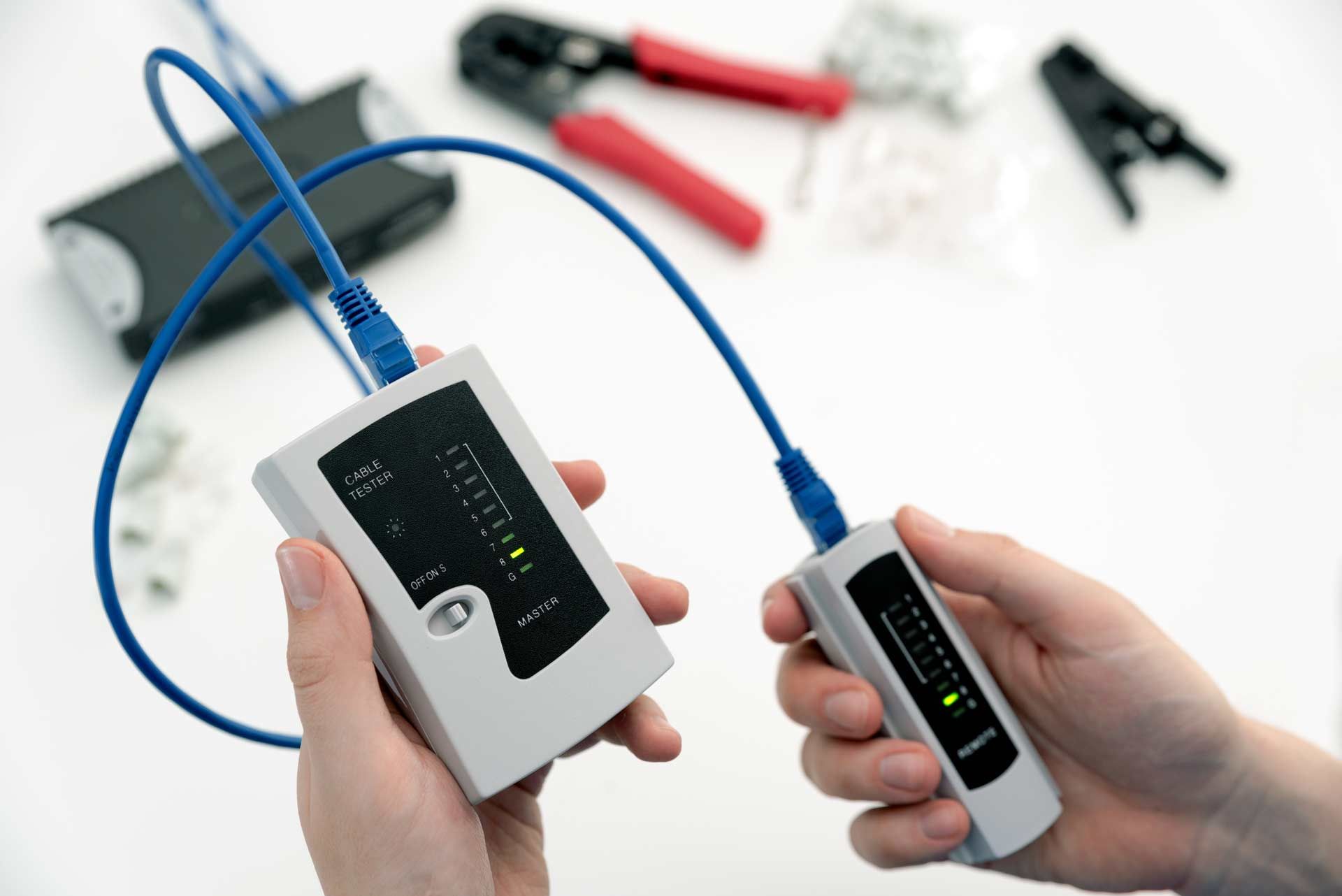 Person holds a network cable tester, connected by a blue cable, to test network connectivity.
