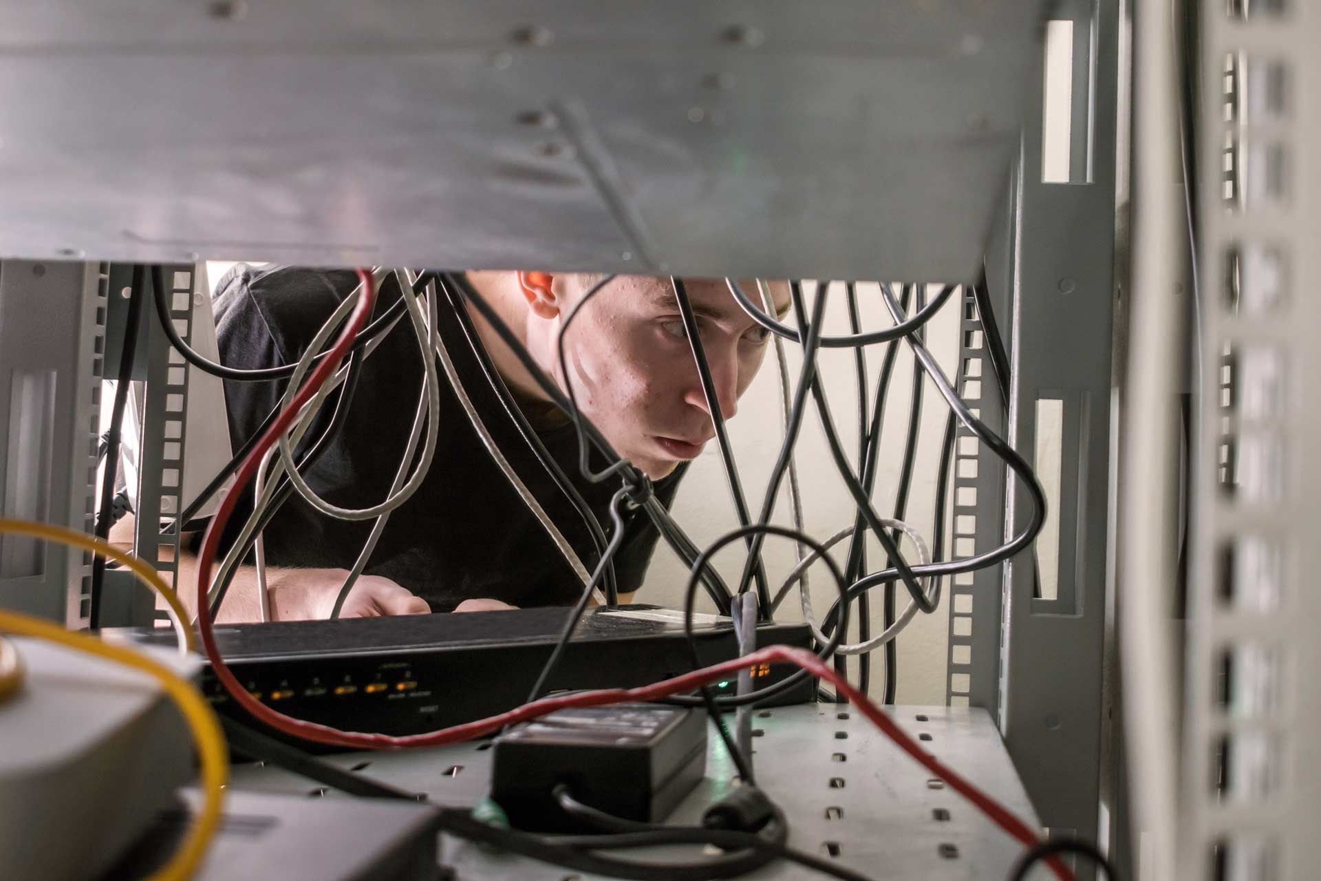 Person looks into open server rack, examining wires and equipment.