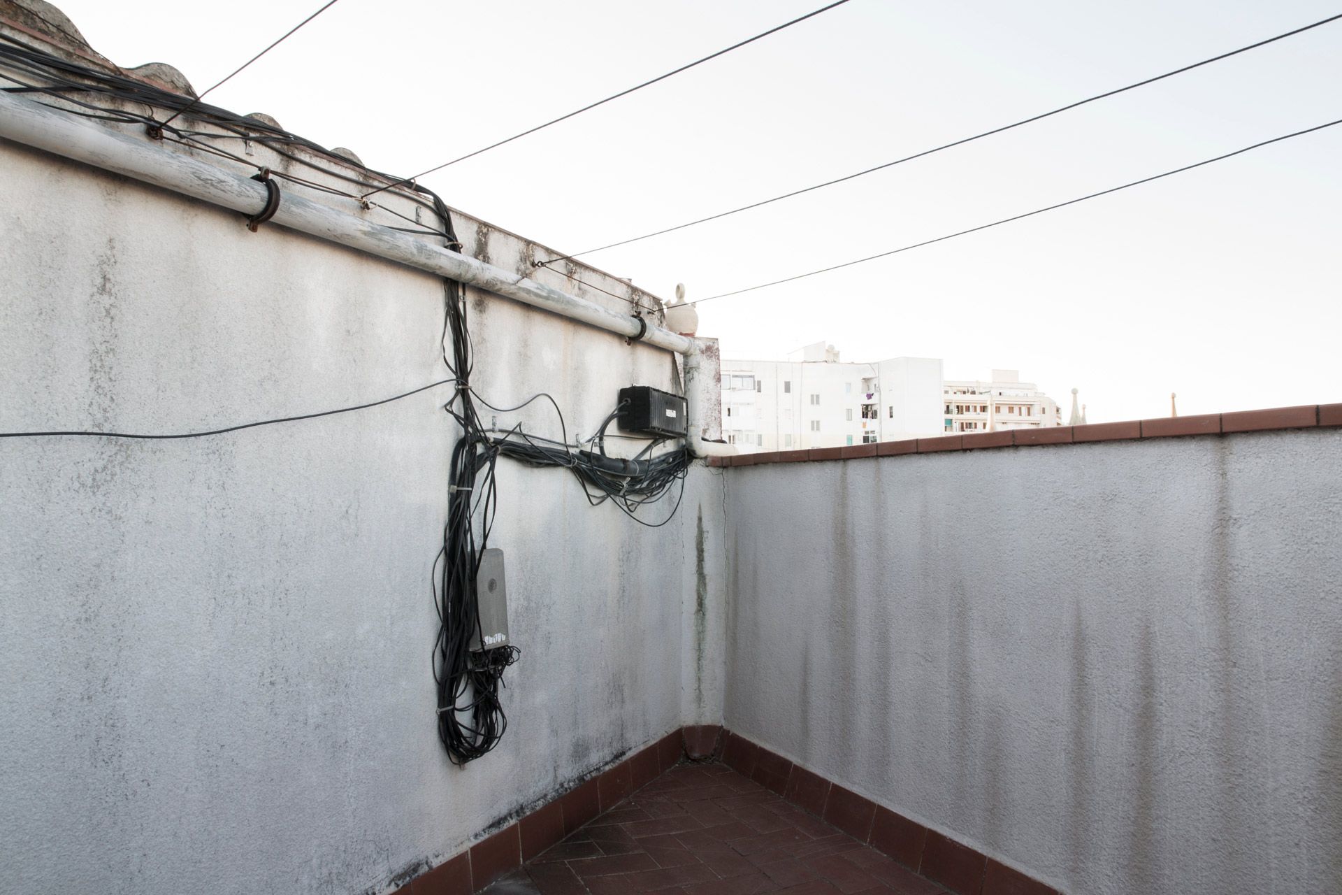 White building corner with tangled electrical wires. Overhead wires and other buildings are in the background.
