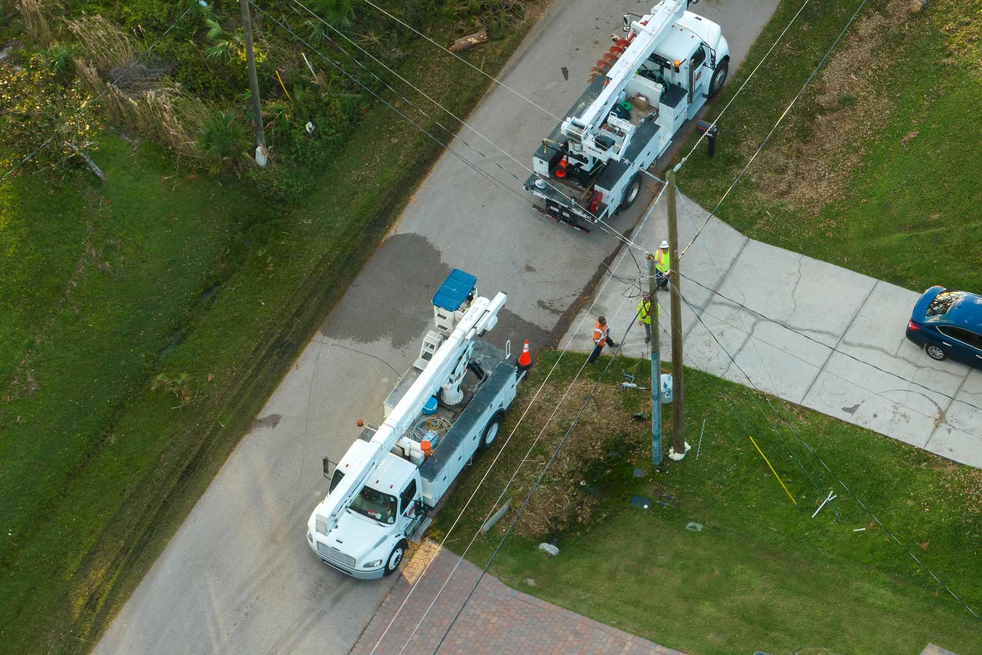 Two utility trucks with raised booms near a utility pole on a residential street.
