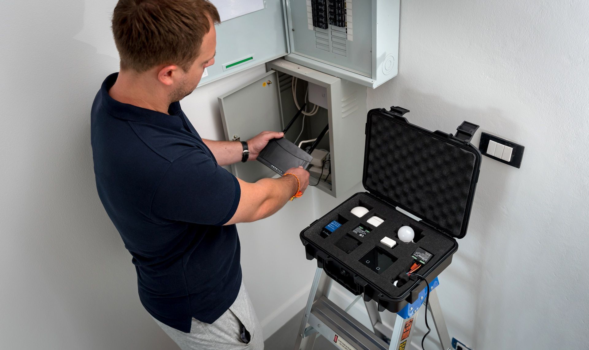Man working on electrical panel, tools open in case on step ladder in a white room.