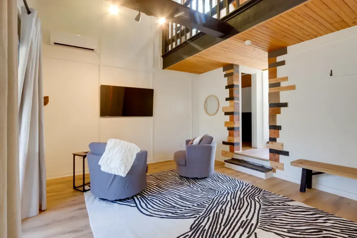 A living room with two chairs , a rug and a flat screen tv.