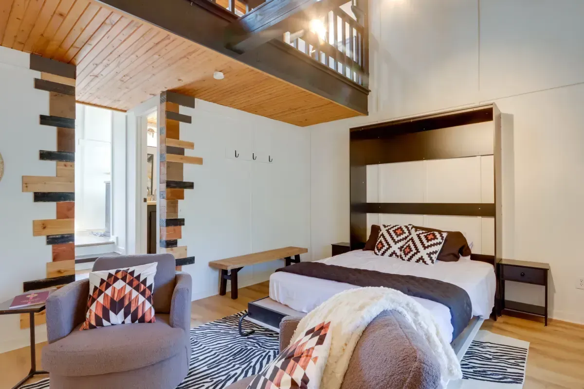 A bedroom with a bed , chair , rug and stairs.
