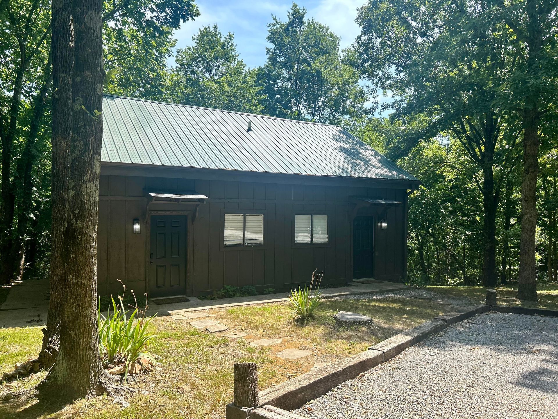 A small house with a green roof is surrounded by trees and gravel.