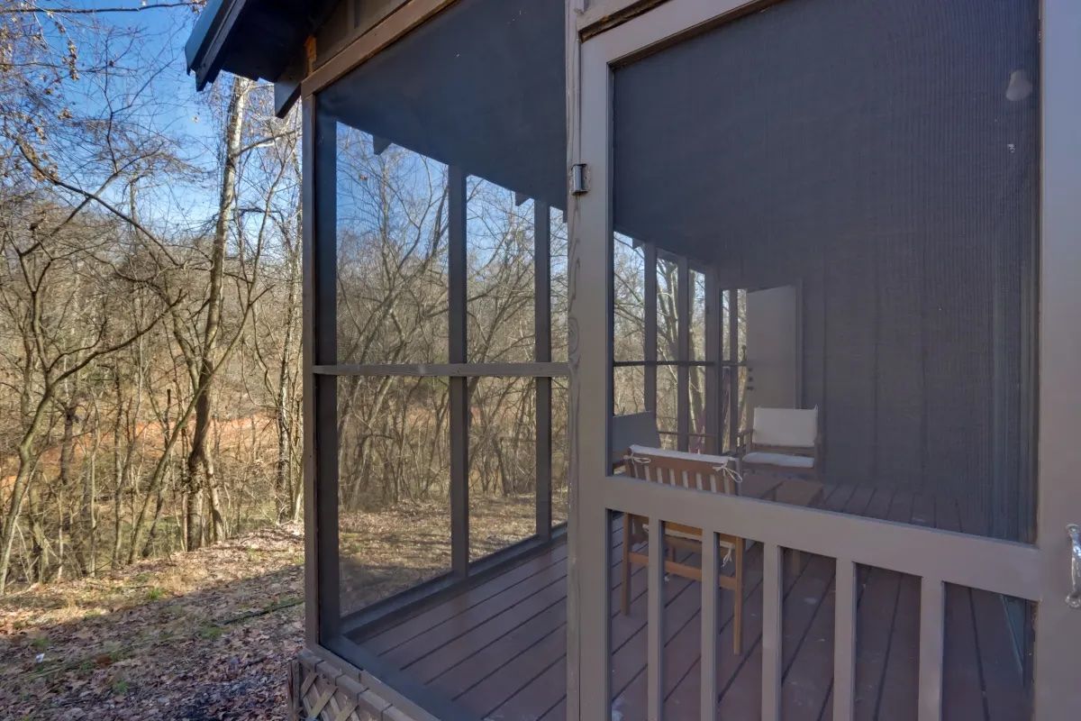 A screened in porch with a view of the woods.