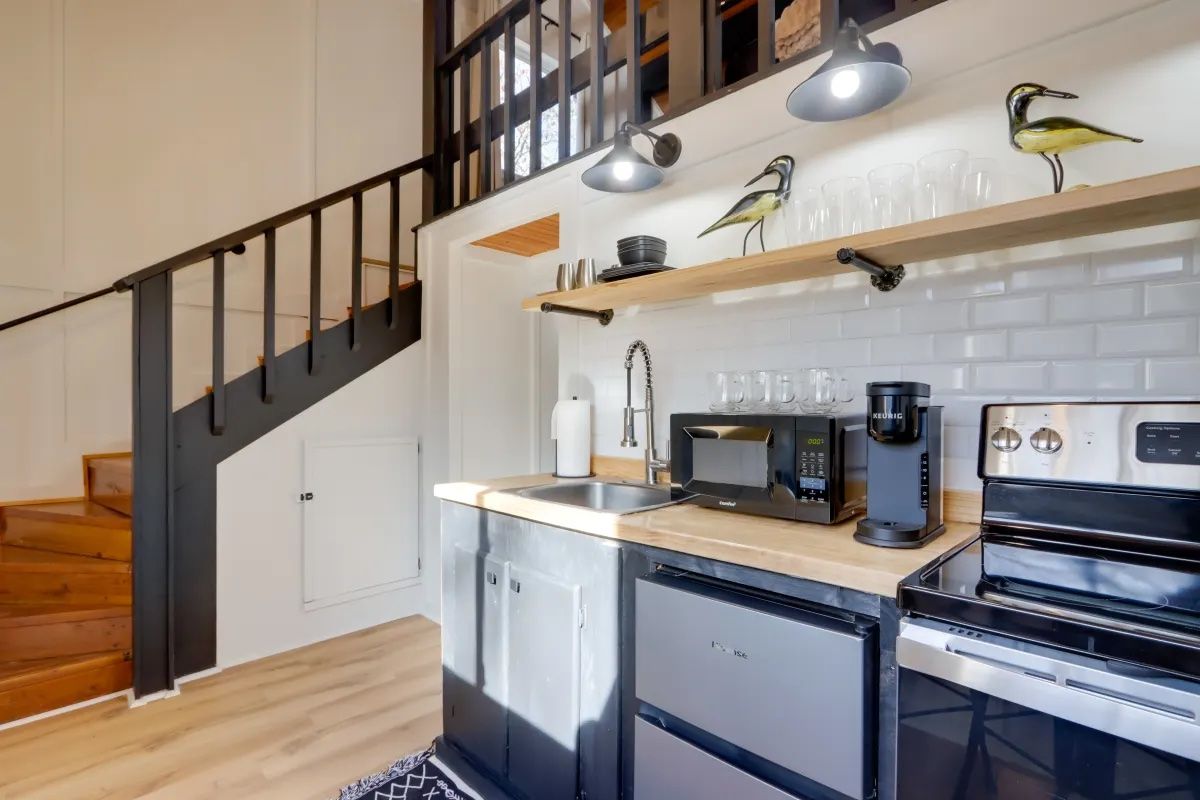 A kitchen with a stove , sink , microwave and stairs.