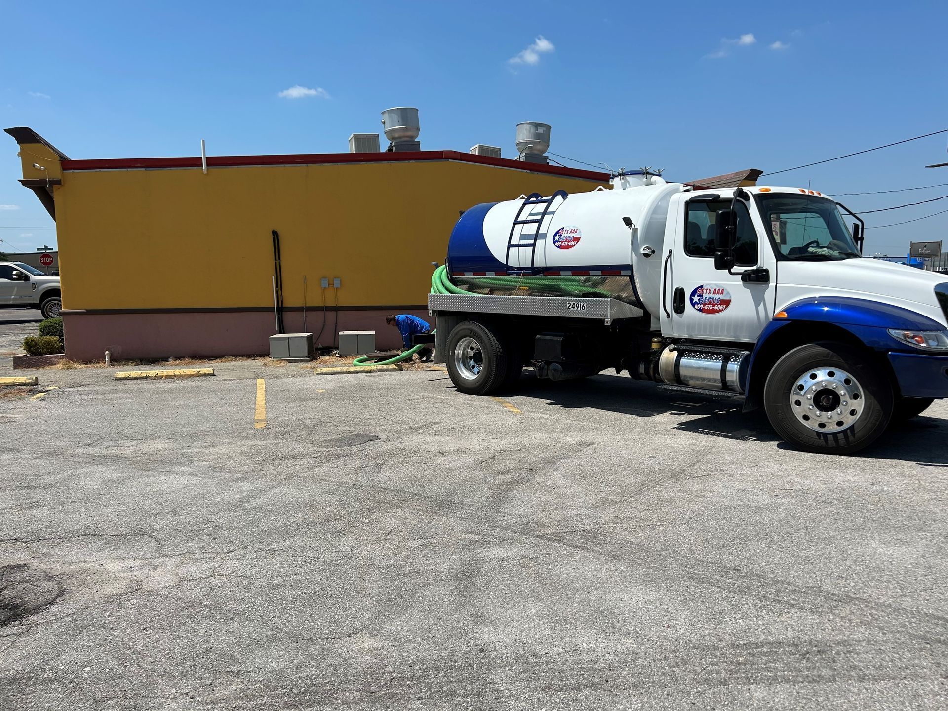 White tanker truck parked beside a yellow building on a gravel lot under a bright sky.