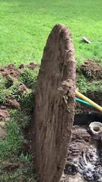Mud fountain erupting from a narrow pipe in a grassy yard, with muddy water splashing around it