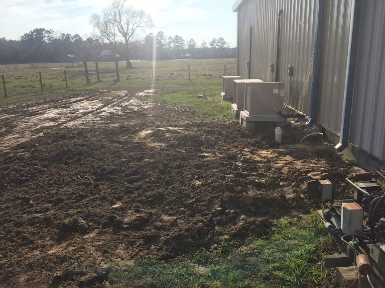 Mud-covered yard beside a metal building with farm equipment and a fence in the background