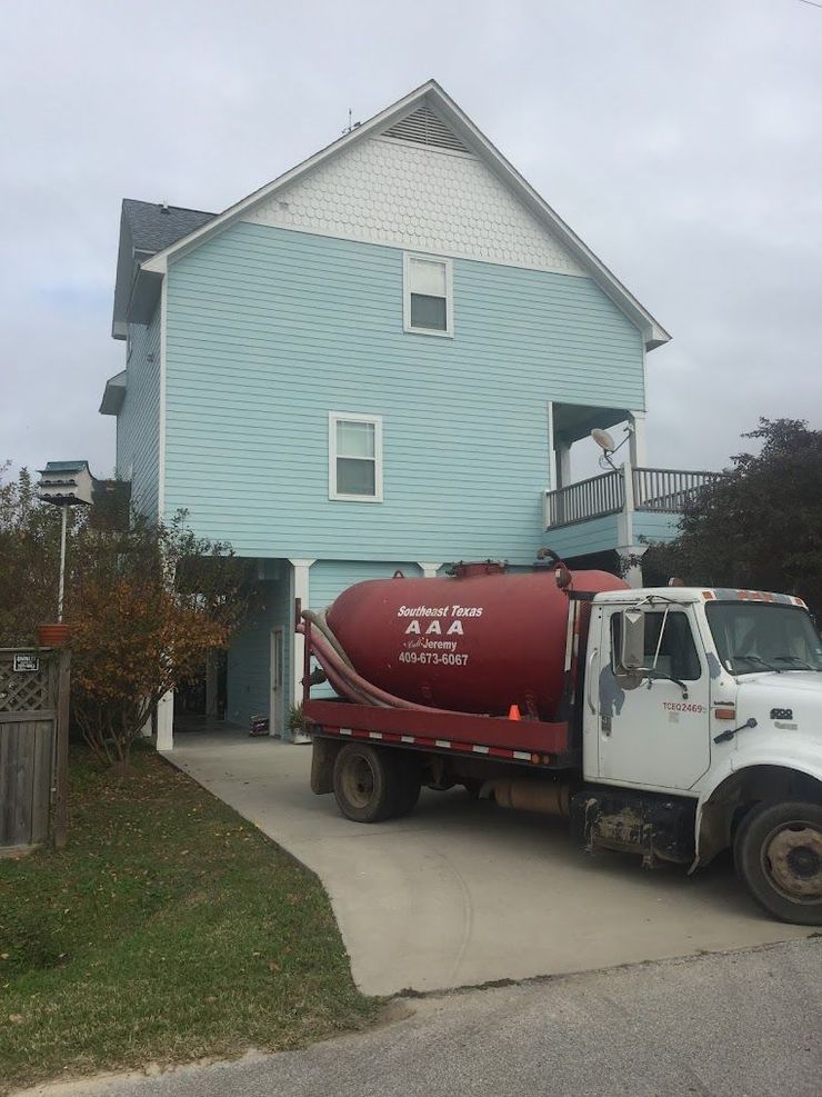 Red cement truck parked in a driveway beside a light blue house with a steep roof.