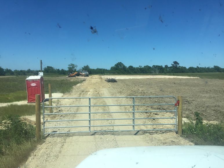 Rural dirt road with a metal gate, red mailbox, and open field under a clear blue sky