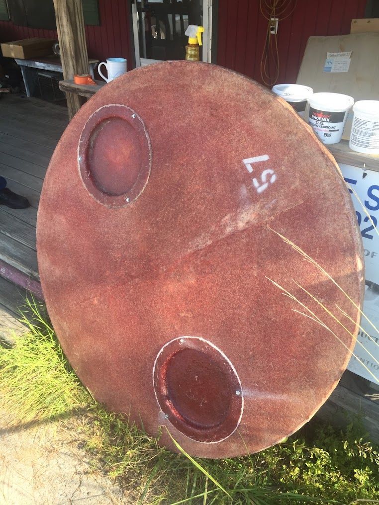 Large rusted metal cylinder or tank with two circular ports, sitting outdoors near workshop items.