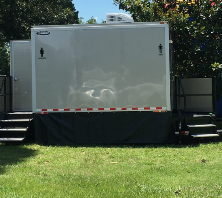 White trailer in a grassy yard, flanked by black steps and trees in the background.