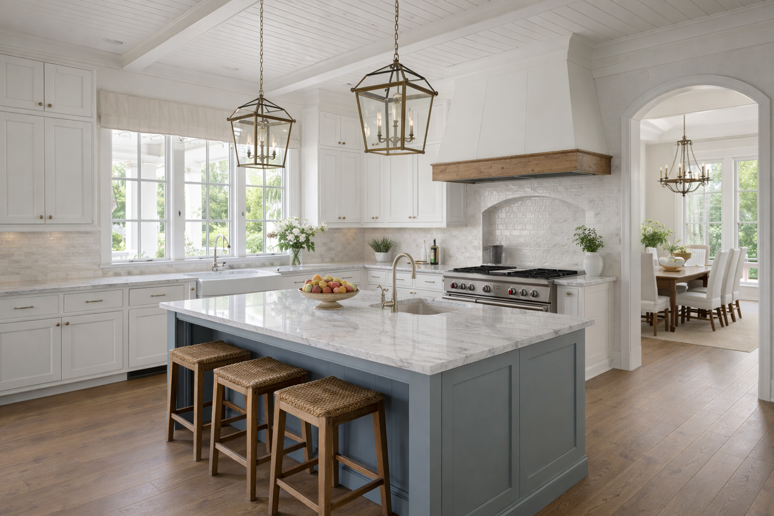 A white kitchen with a blue island, marble countertops, three woven stools, and two hanging lantern-style light fixtures.