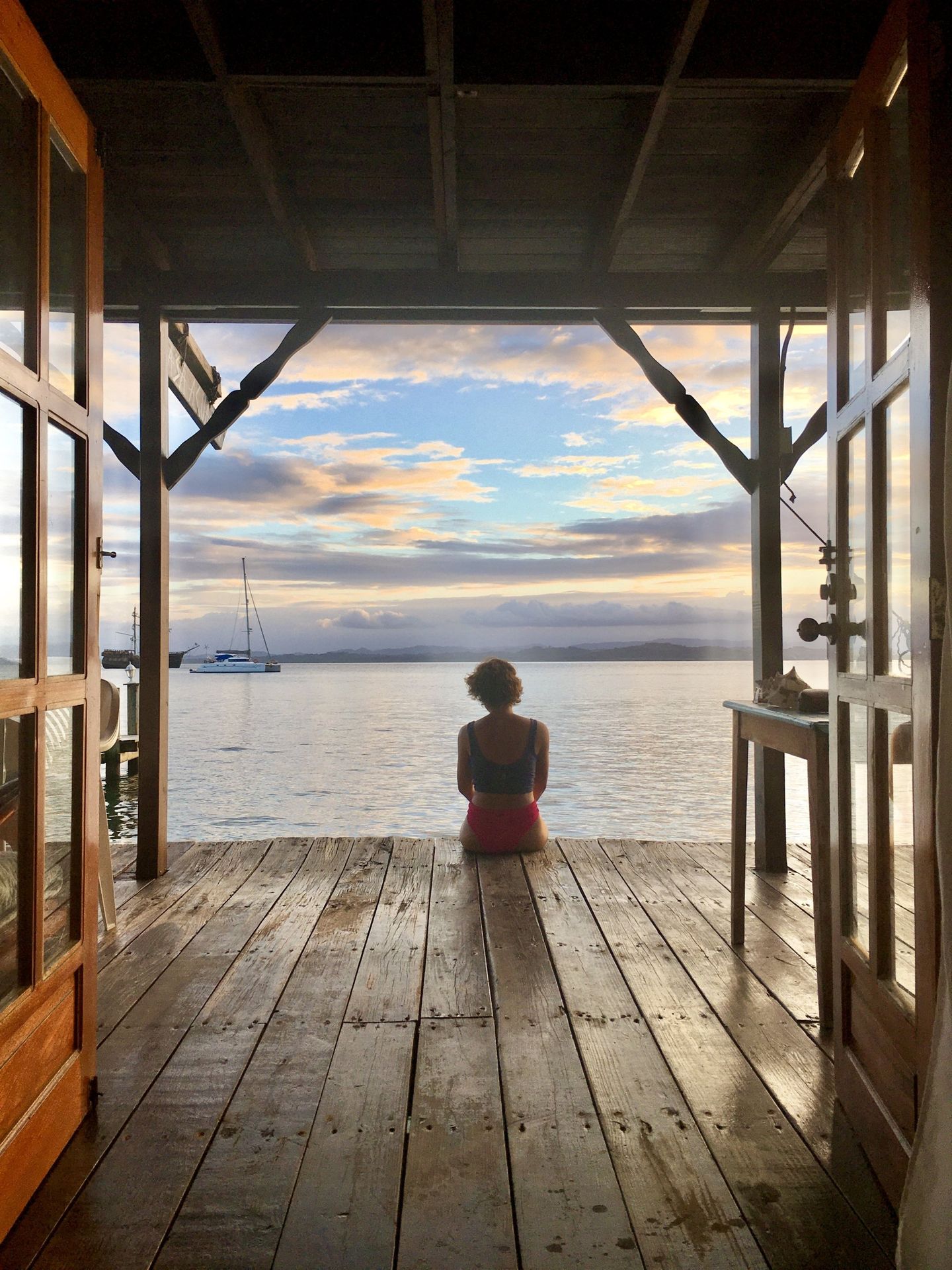 A woman is sitting on a wooden deck overlooking the ocean.