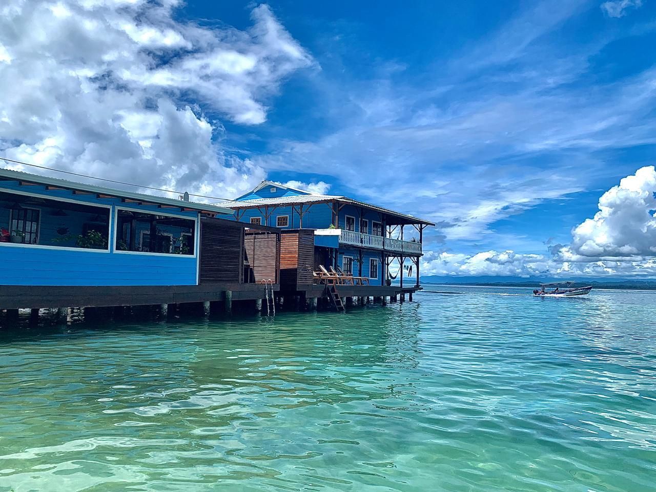 Blue overwater bungalow by clear turquoise sea under a bright, cloudy sky