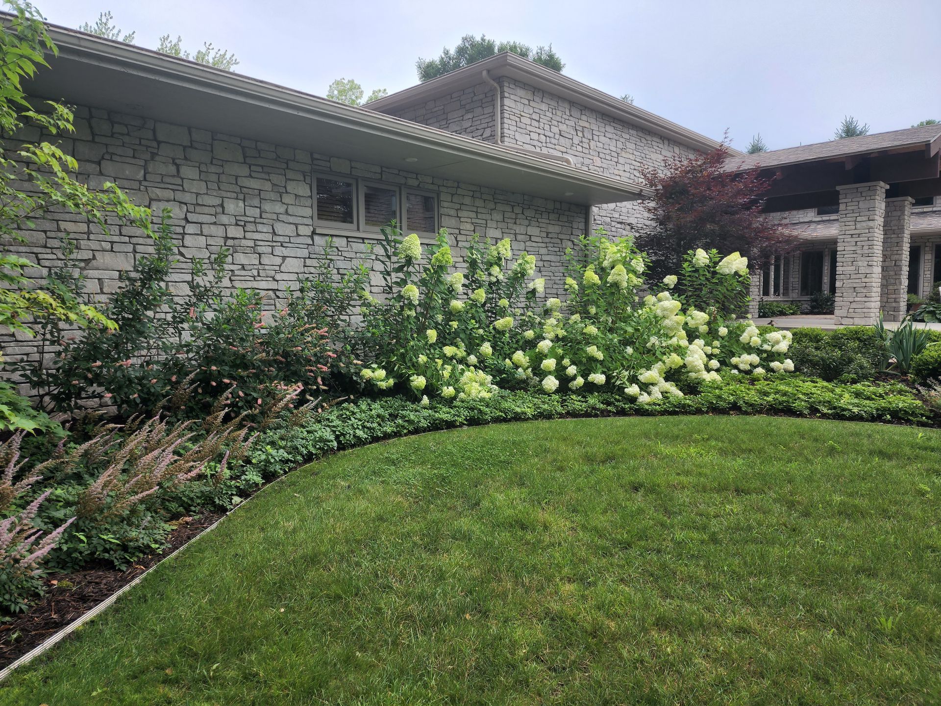 Stone house with a lush green lawn and flowering garden shrubs under a cloudy sky